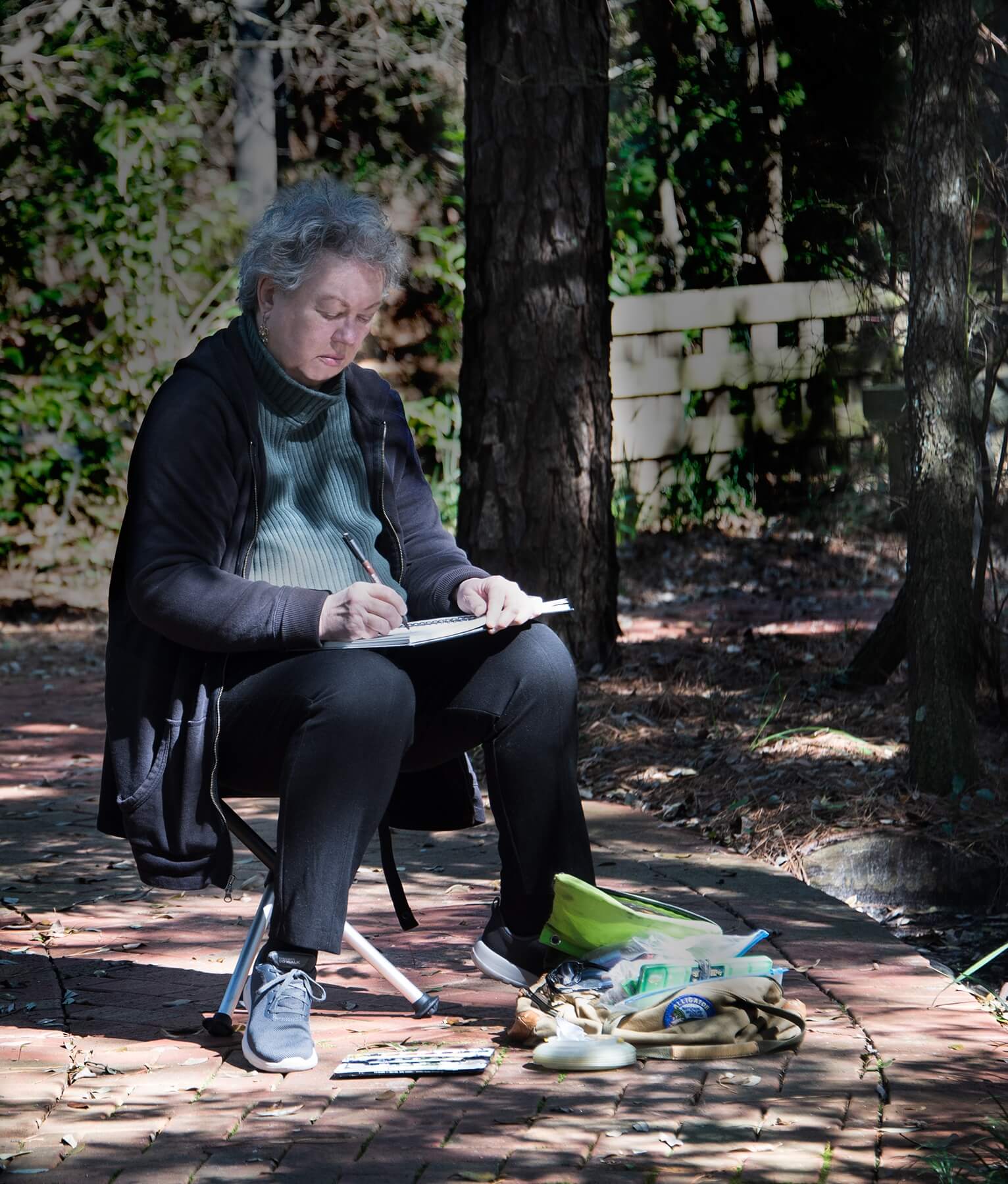 E.M. Corsa sitting outside by a tree sketching her surroundings.