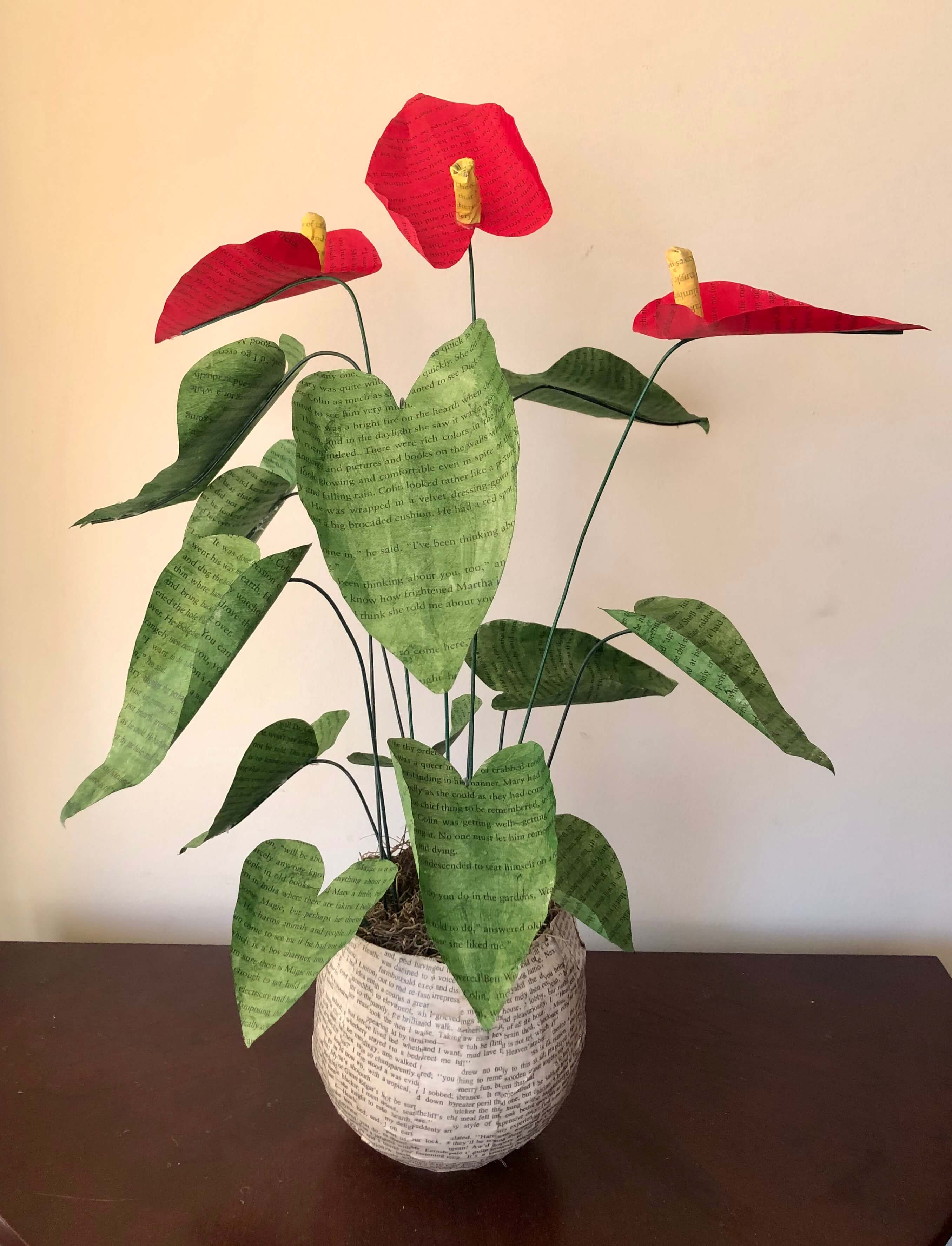 Paper flower art. Allegra Murray, a paper artist, crafted a potted red paper lily with green leaves and yellow stamen in a paper pot. 