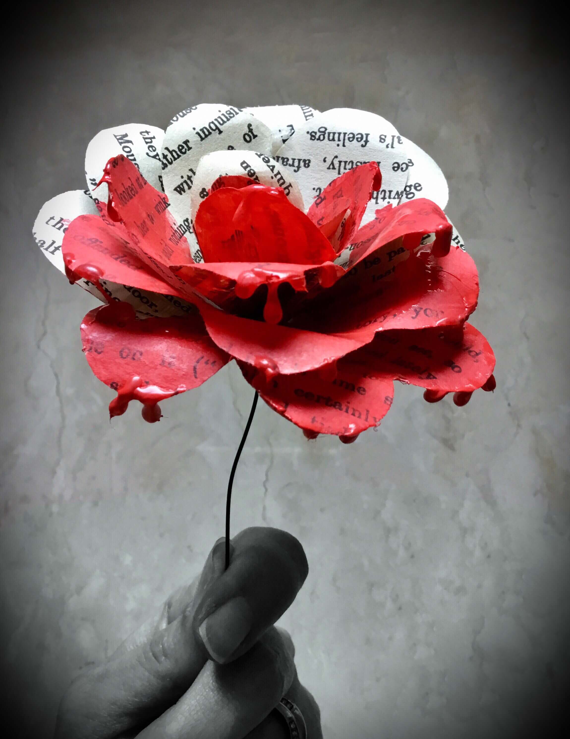 A photo of a paper flower made from book pages. It is red on one half and black and white on the other. 