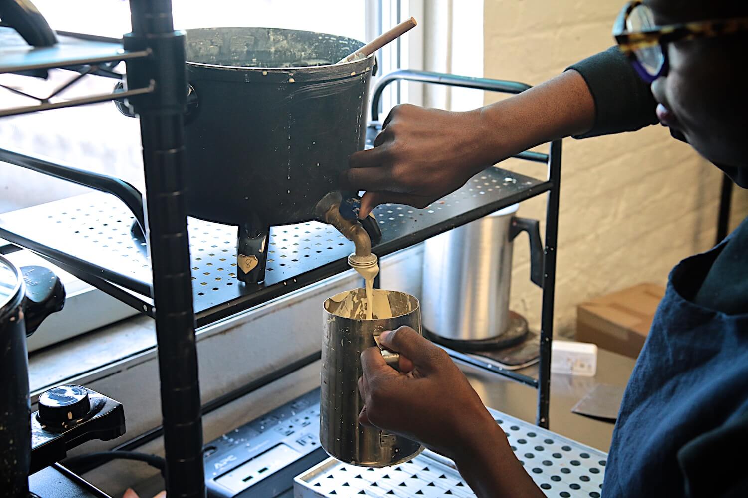 Imagine of Sabine filling a stainless steel pitcher with melted wax from a large wax melter.